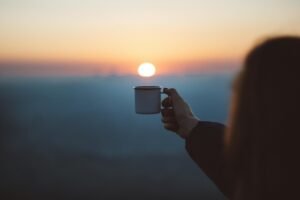 pexels-photo-1752806-1752806 A person holds a coffee cup against a beautiful sunrise, capturing a serene outdoor moment.